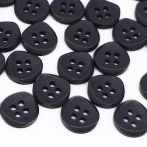May include: A large group of black plastic buttons with four holes each. The buttons are shaped like a rounded triangle.