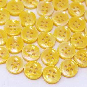 May include: A large group of yellow buttons with four holes each. The buttons are made of a shiny, pearlescent material.