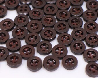 May include: A large pile of brown wooden buttons with four holes each. The buttons have a slightly reddish hue and are scattered on a white surface.