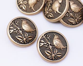 May include: A group of ten gold-toned buttons with a bird and floral design. The buttons are round and have a raised design.