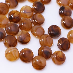 以下が含まれることがあります： 茶色と白のマーブル模様の丸いボタンのセット。ボタンは滑らかで光沢があります。