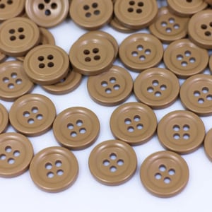 Könnte beinhalten: Eine große Gruppe brauner Plastikknöpfe mit jeweils vier Löchern. Die Knöpfe sind in einem zufälligen Muster auf einer weißen Oberfläche angeordnet.