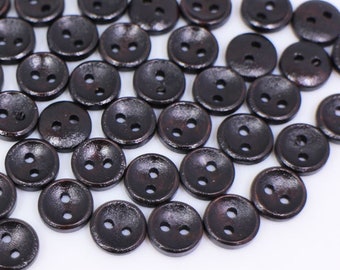 May include: A large group of dark brown wooden buttons with two holes each. The buttons are scattered on a white surface.