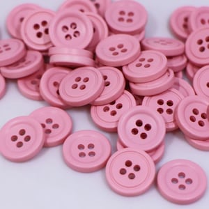 Könnte beinhalten: Ein großer Haufen rosa Knöpfe mit jeweils vier Löchern. Die Knöpfe sind aus einem glatten, matten Material gefertigt.