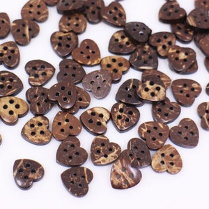 Peut inclure: Une collection de boutons en forme de cœur en coquille de noix de coco de couleur marron. Les boutons ont un motif de grain de bois naturel et plusieurs trous pour la couture.