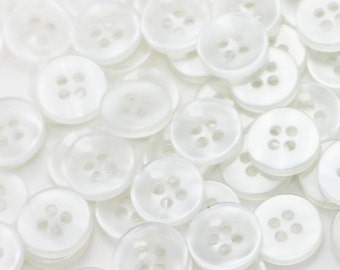 May include: A large pile of white plastic buttons with four holes each. The buttons are arranged in a random pattern.