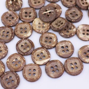 May include: A collection of brown coconut shell buttons with four holes each. The buttons are scattered on a white surface.