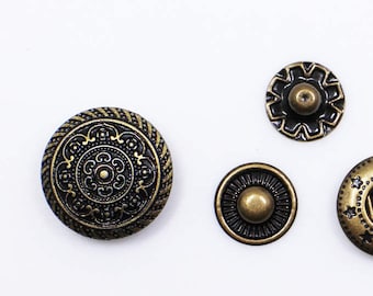 May include: Four antique gold-toned metal buttons with intricate designs. Two buttons have a circular design with a raised center, one has a starburst design, and one has a floral design.