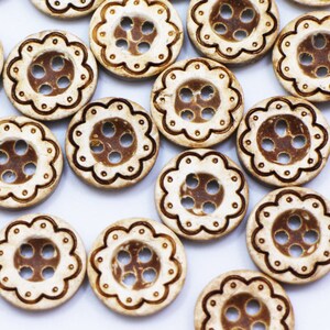 May include: A collection of white coconut shell buttons with a brown decorative design. The buttons have four holes and are arranged in a random pattern on a white surface.