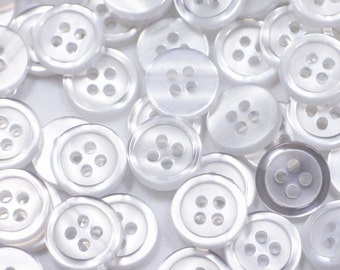 May include: A large pile of white plastic buttons with four holes each. The buttons are scattered on a white surface.