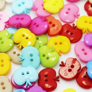May include: Assortment of colorful plastic apple-shaped buttons with two holes each. The buttons are in various colors, including red, yellow, blue, green, pink, and white.