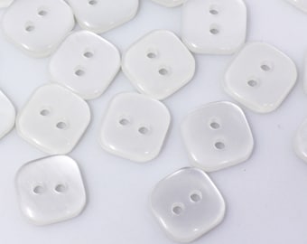May include: A collection of white, two-hole, square-shaped buttons. The buttons are made of a smooth, shiny material.