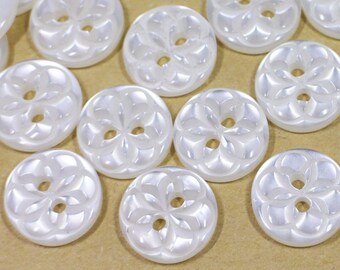 Könnte beinhalten: Eine Sammlung weißer Plastikknöpfe mit einem Blumenmuster. Die Knöpfe haben zwei Löcher und sind in einem zufälligen Muster angeordnet.