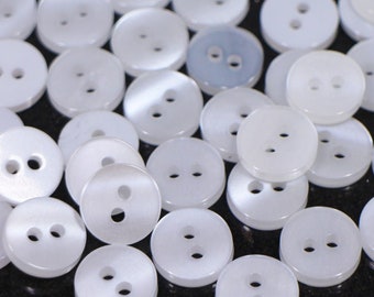 May include: A pile of white, two-hole buttons. The buttons are round and have a smooth, shiny finish.