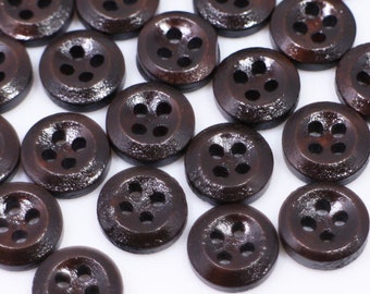 May include: A collection of brown wooden buttons with four holes each. The buttons are arranged in a random pattern on a white surface.