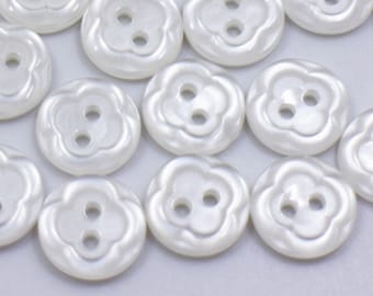 Könnte beinhalten: Eine Sammlung weißer perlmuttartiger Knöpfe mit einem Kleeblatt-Design. Die Knöpfe haben zwei Löcher.