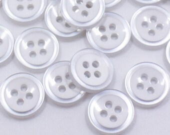 May include: A collection of white plastic buttons with four holes each. The buttons are scattered on a white surface.
