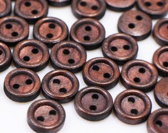 May include: A large group of brown wooden buttons with two holes each. The buttons are scattered on a white surface.