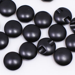 May include: A collection of black plastic buttons with a raised design on the top. The buttons are round and have a smooth, glossy finish.