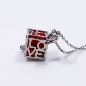 May include: A silver chain necklace with a red cube pendant that says "LOVE" in a cutout design.