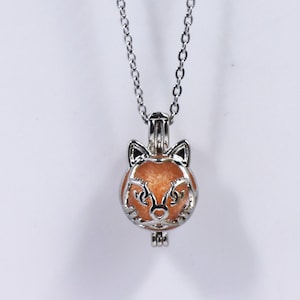 May include: A silver chain necklace with a silver fox-shaped charm. The charm has a clear glass orb inside with a light orange shimmer.