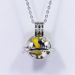 May include: A silver necklace with a round charm featuring a silhouette of two cats. The charm is hollow and has a yellow interior.