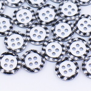 May include: A collection of black and white checkered buttons with four holes each. The buttons are arranged in a pile on a white surface.