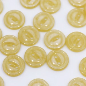 May include: A collection of yellow plastic buttons with two holes each. The buttons are scattered on a white surface.