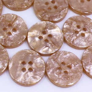 Peut inclure: Un ensemble de boutons à 4 trous de couleur brun clair avec un effet marbré. Les boutons sont ronds et ont une finition lisse et brillante.