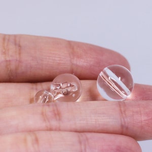May include: Three clear glass beads with a subtle pink hue. The beads are round and have a smooth, polished finish.