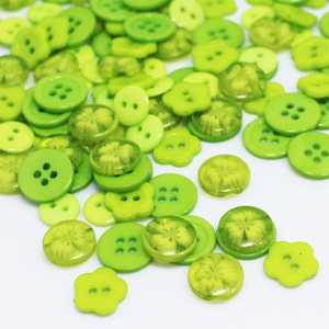 May include: A collection of green plastic buttons in various sizes and shapes, including some with a four-leaf clover design.