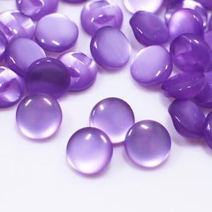 Peut inclure: Un grand groupe de boutons en plastique violet. Les boutons sont ronds et ont une finition brillante.
