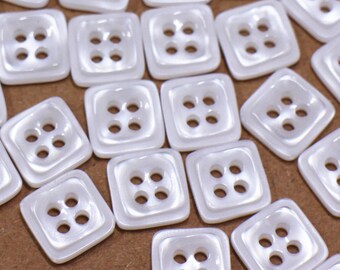 May include: A collection of white, square-shaped buttons with four holes each. The buttons have a slightly iridescent finish.