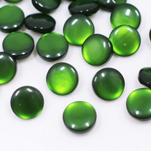May include: A collection of green round buttons with a shiny finish. The buttons are scattered on a white surface.