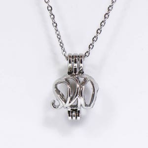 May include: A silver necklace with a delicate chain and a pendant shaped like an elephant. The pendant is open and appears to be designed to hold a small object, such as a pearl.