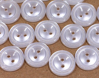 May include: A collection of white plastic buttons with two holes each. The buttons have a raised, rounded centre and a decorative rim.