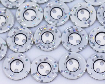 May include: A collection of white buttons with a silver iridescent finish and two holes. The buttons are scattered on a white surface.