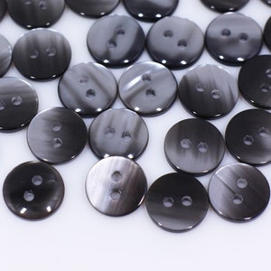 以下が含まれることがあります： 黒とグレーの2穴ボタンのセット。ボタンは丸型で、滑らかで光沢のある仕上げです。