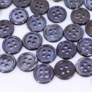 Peut inclure: Un grand nombre de boutons gris foncé à quatre trous. Les boutons sont faits d'un matériau lisse et brillant.