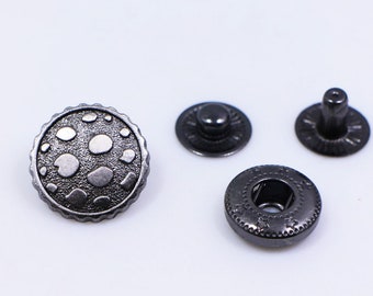 May include: A set of three black metal snap fasteners. The top fastener has a decorative design with a raised pattern of circles. The other two fasteners are plain.