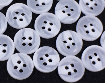 May include: A pile of white plastic buttons with a swirl pattern. The buttons have four holes each.