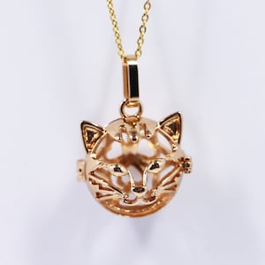 May include: Gold necklace with a cat-shaped charm. The charm is a hollow sphere with a cat's face cut out.
