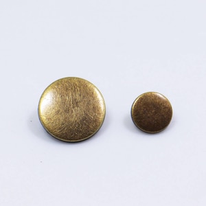 May include: Two round, flat, brass buttons. The larger button is approximately 2.5 cm in diameter. The smaller button is approximately 1.25 cm in diameter.