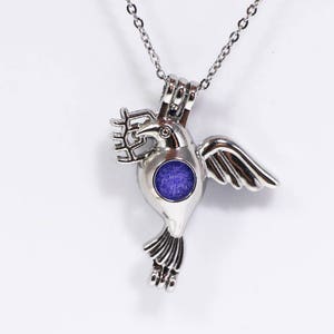 May include: Silver hummingbird charm necklace with a blue glass center. The necklace is on a white background.