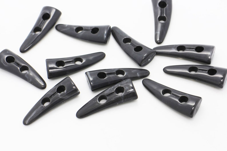 May include: A group of black horn-shaped buttons with two holes each. The buttons are made of a smooth, shiny material and have a slightly curved shape.