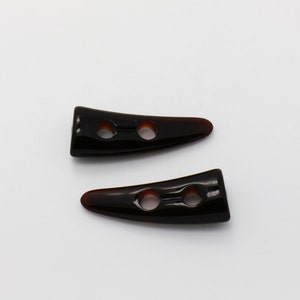 Peut inclure: Deux boutons en plastique en forme de corne noire avec deux trous chacun. Les boutons ont une finition brillante.