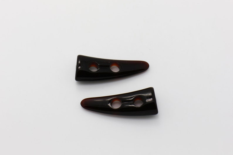 Peut inclure: Deux boutons en plastique en forme de corne noire avec deux trous chacun. Les boutons ont une finition brillante.