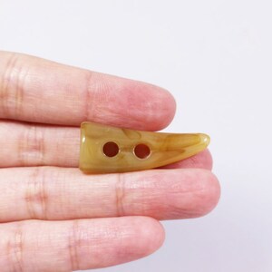 May include: A two-hole horn-shaped button in a light brown color with a marbled pattern.