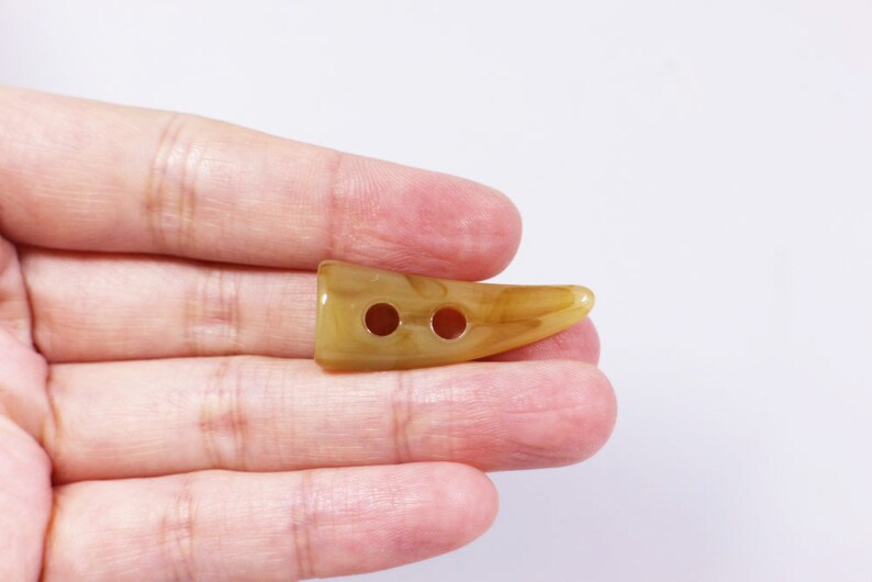 May include: A two-hole horn-shaped button in a light brown color with a marbled pattern.
