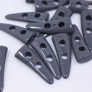 May include: A group of gray plastic buttons with two holes each. The buttons are shaped like a pointed tooth or a horn.